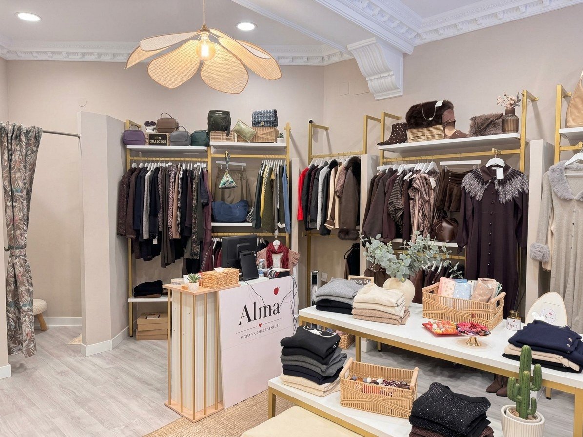 Interior de Alma: percheros dorados con abrigos y vestidos, bolsos en las baldas y mesas con jerséis doblados